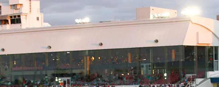 The glass-fronted grandstand of the Hippodrome de Trois-Rivières with spectators along the rail, at dusk