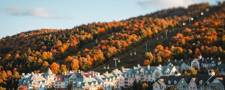 A resort village with pastel facades at the foot of a ski hill in autumn colours, with a gondola line